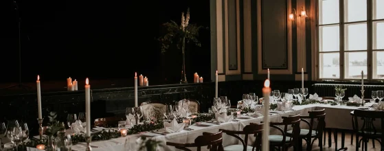 Salle de réception élégamment décorée avec des tables dressées, des chandelles allumées et une ambiance tamisée.
