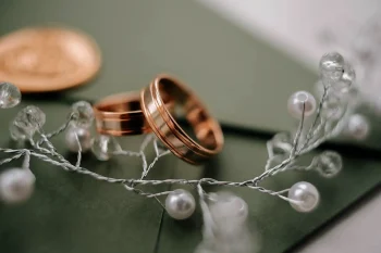 Deux alliances en or rose posées sur une enveloppe verte, entourées de guirlandes de perles et de lumière.