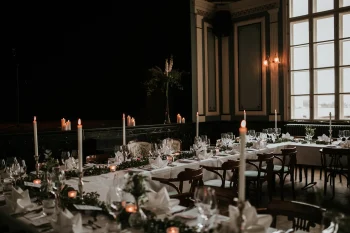 Salle de réception élégamment décorée avec des tables dressées, des chandelles allumées et une ambiance tamisée.
