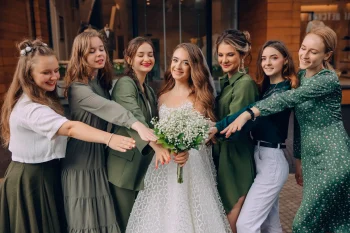 Une mariée entourée de ses demoiselles d'honneur, toutes vêtues de nuances de vert, posant joyeusement avec son bouquet.