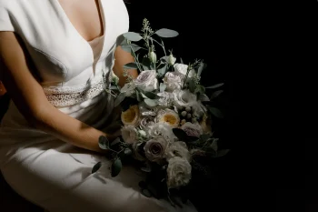 Gros plan sur une mariée en robe blanche tenant un bouquet de fleurs pastel sous un éclairage dramatique.