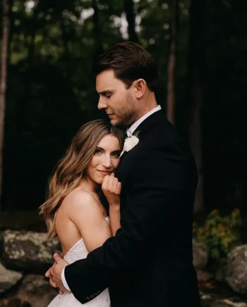 Un couple de jeunes mariés partage un moment tendre en pleine nature, la mariée souriante blottie contre son époux.